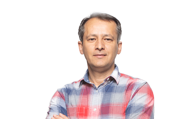 A middle-aged male of Middle Eastern descent is posing with his arms crossed. A white backdrop is behind him. He wears a red, blue, and grey flannel dress shirt.