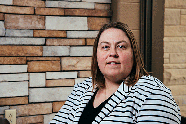 Middle-aged woman with shoulder-length brown hair looking at the camera wearing a white jacket with black stripes, and a black shirt. 